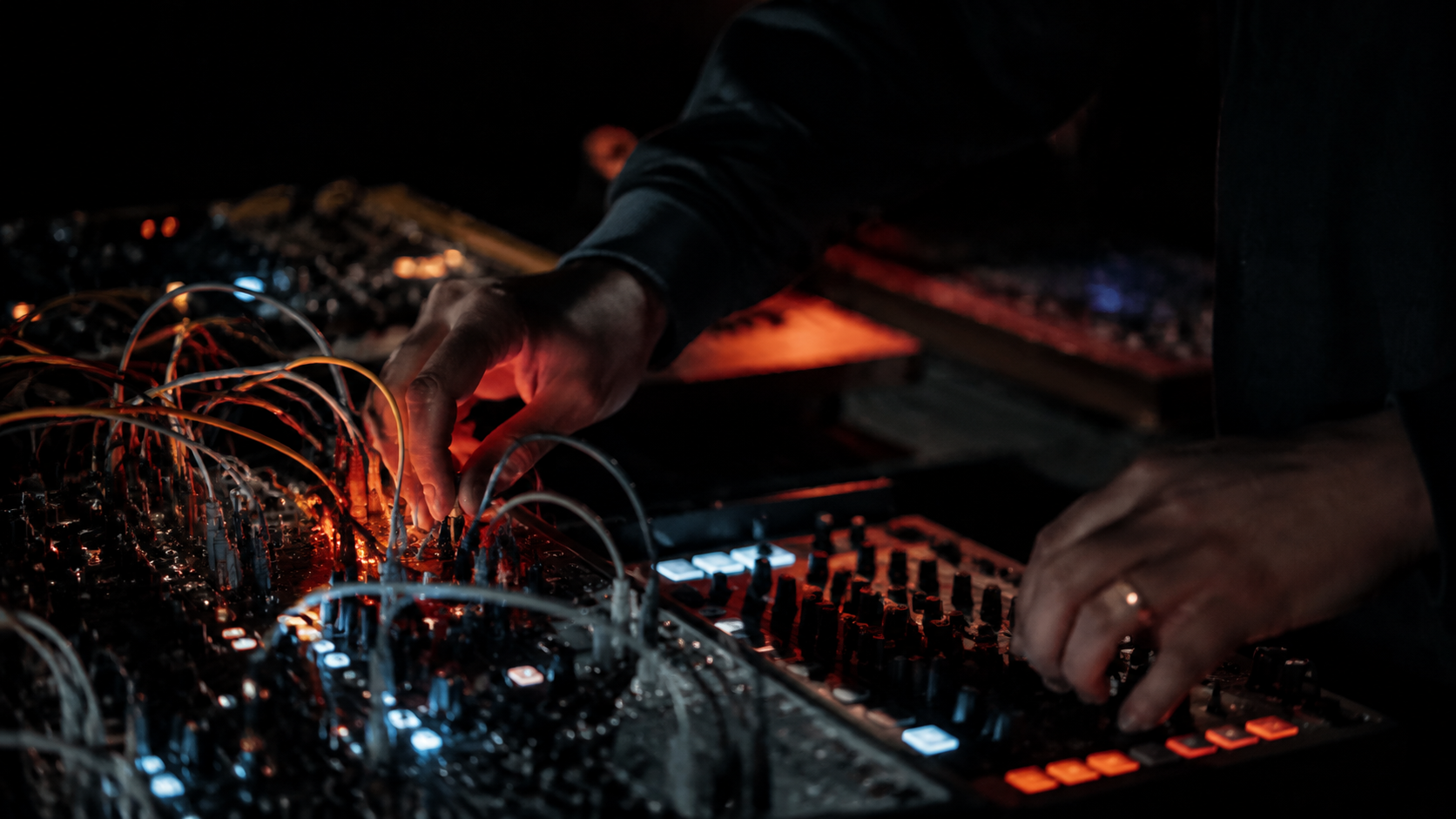 Hands shaping sound on a modular synthesizer and mixing desk